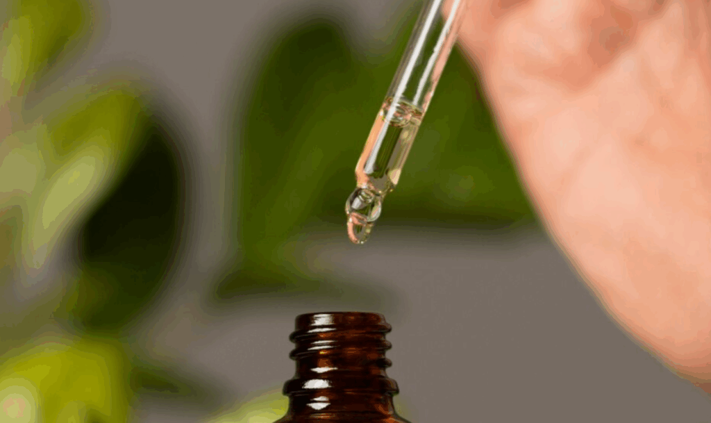 Close-up of a dropper releasing pure rose oil into a glass bottle.